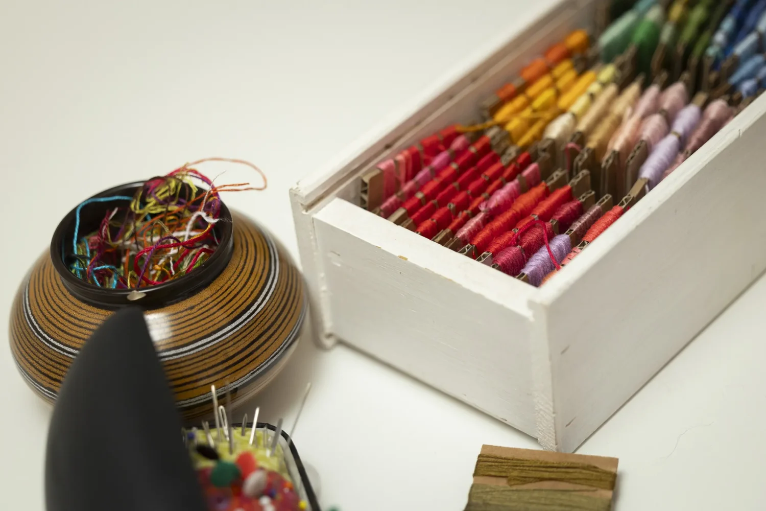 Kirjontalankoja laatikossa ja keramiikkakipossa lankojen tähteitä.